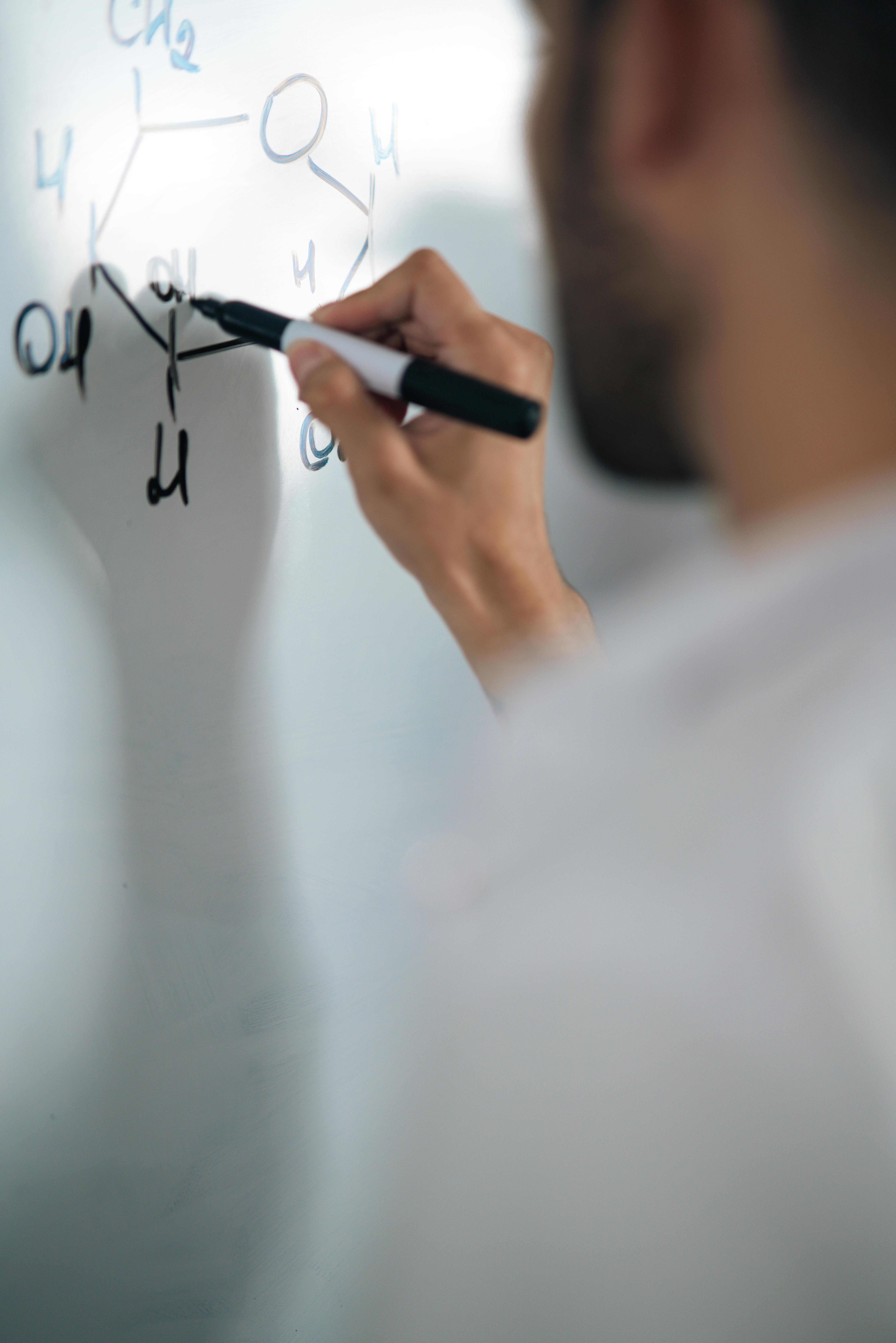 A chemist writing a molecular structure on a whiteboard with a marker, close-up view.